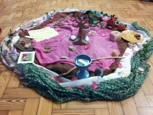 An altar created on the floor using pink, green and white cloths, including a goddess figurine, a cup of water, and many other items