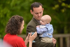 A baby, held by its father, is blessed with Water by Celebrant Keli Tomlin