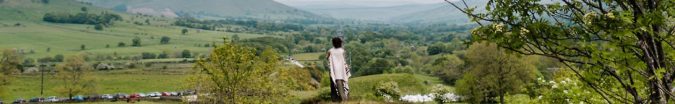 A woman stands with her back to the camera looking out a the Edale Valley