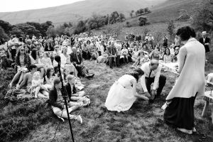 A bride and groom plant a tree as their guests look on, Celebrant Keli Tomlin is watching. The image is in black and white.
