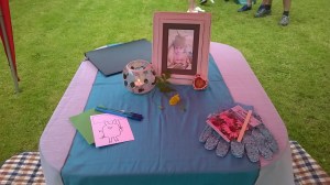 A Baby Naming altar including a photograph, a candle in a glass holder, gardening gloves, paper and pen and yellow flowers
