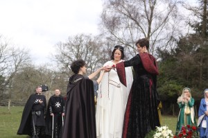 Two Brides dressed in medieval clothes stand beside Pagan Celebrant Keli Tomlin as she performs a Handfasting for them