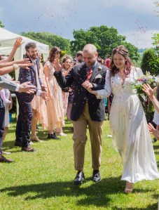 The Bride and Groom walk amongst their guests in a cloud of confetti, they are laughing