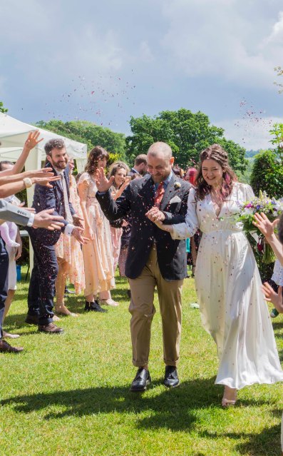 The Bride and Groom walk amongst their guests in a cloud of confetti, they are laughing
