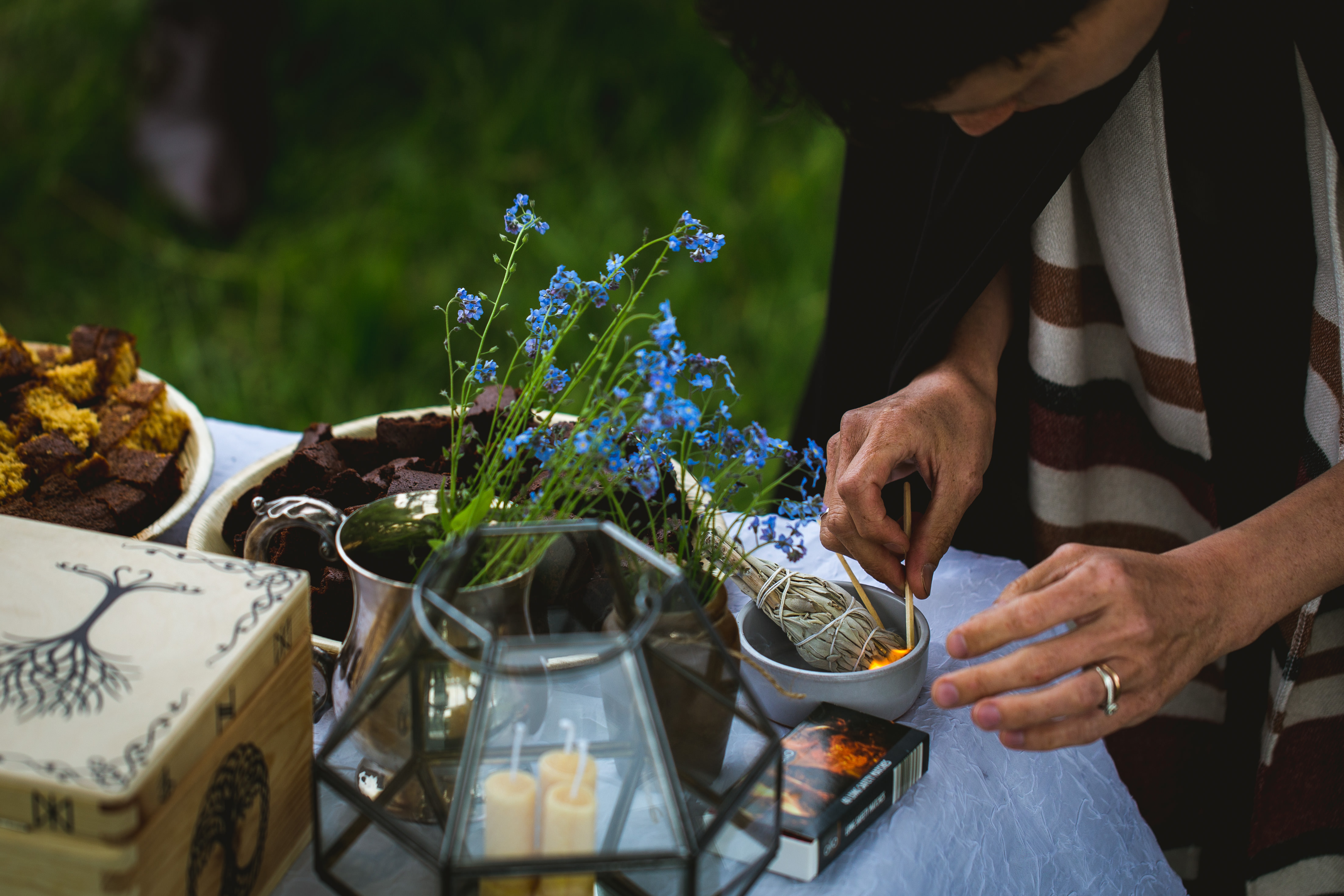 The corner of a pagan wedding altar including forget me knots, beeswax candles and cake. The Celebrant Keli Tomlin lighting a sage bundle for smudging.