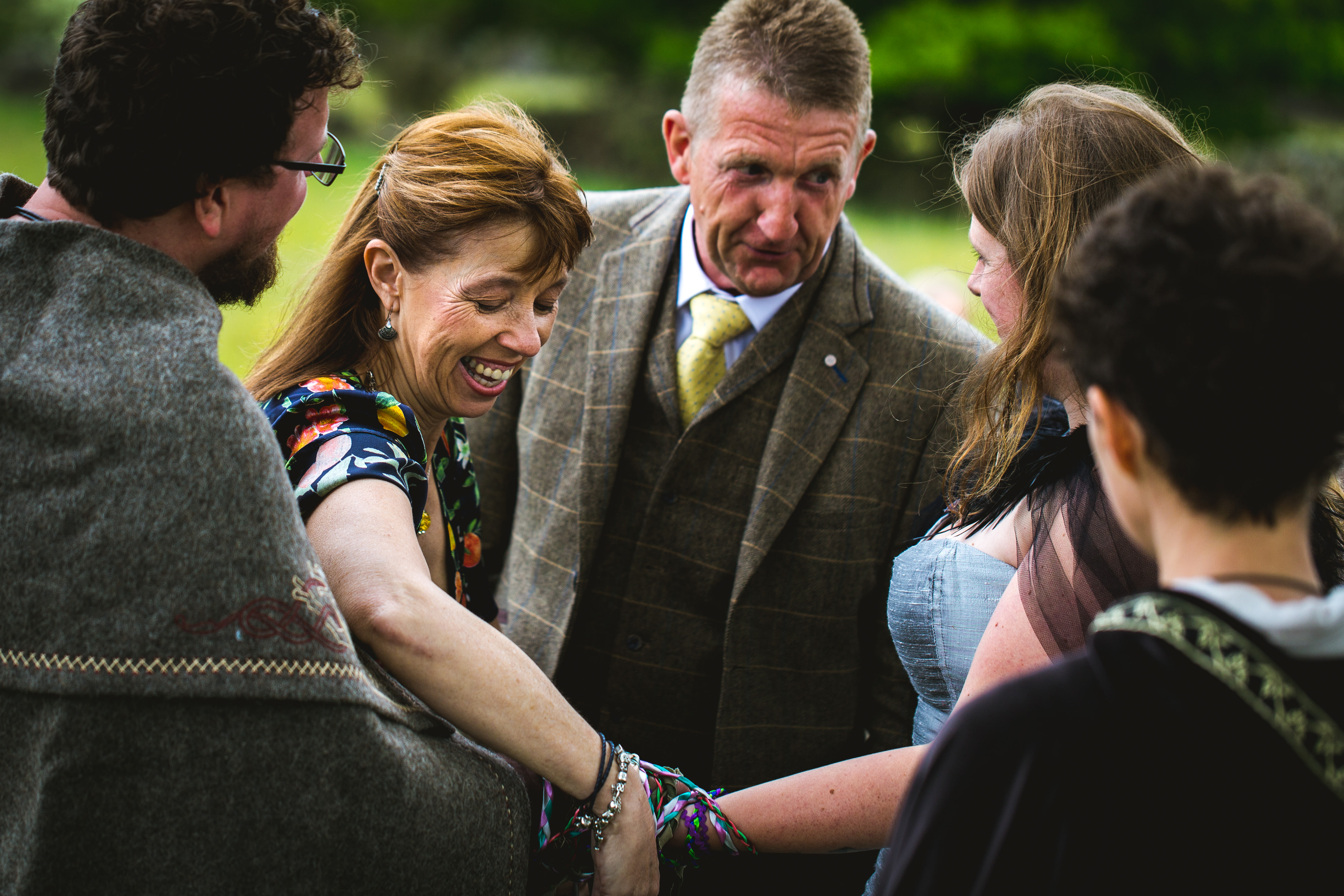 A viking bride and groom have their hands bound together with blue and purple robbons as part of a handfasting lead by Celebrant Keli Tomlin. Everyone is smiling.