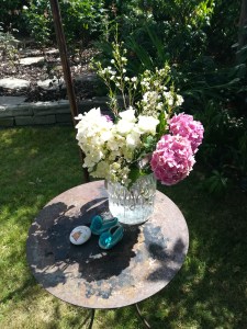 An altar set for a Naming Day Ceremony led by Keli Tomlin including a vase of hydrangea, two small baby shoes and a pebble painted with a cat.