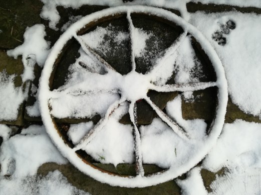 A wooden wheel laid on the ground covered in snow