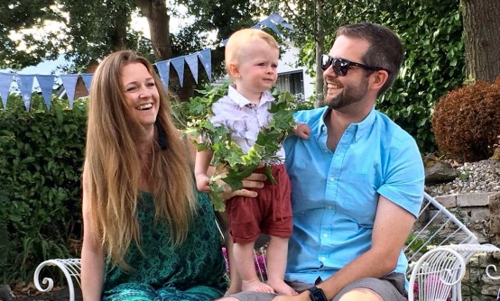 A child stands on his father's knee while his mother looks on smiling during his Naming Day by Keli Tomlin Ceremonies